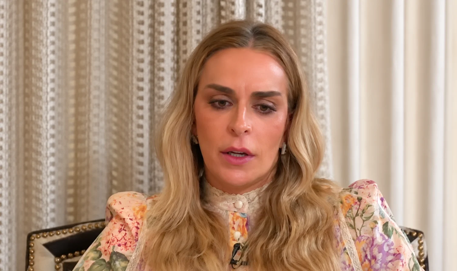 Mulher concede entrevista sentada diante de uma cortina