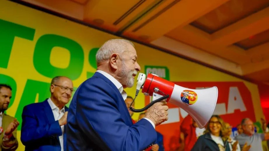 Lula fala ao megafone em evento de campanha, com Geraldo Alckmin ao fundo