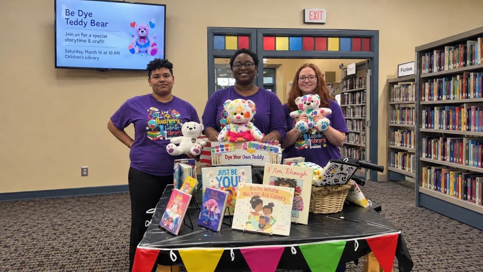 Bibliotecárias ao lado de vitrine de livros infantis em biblioteca
