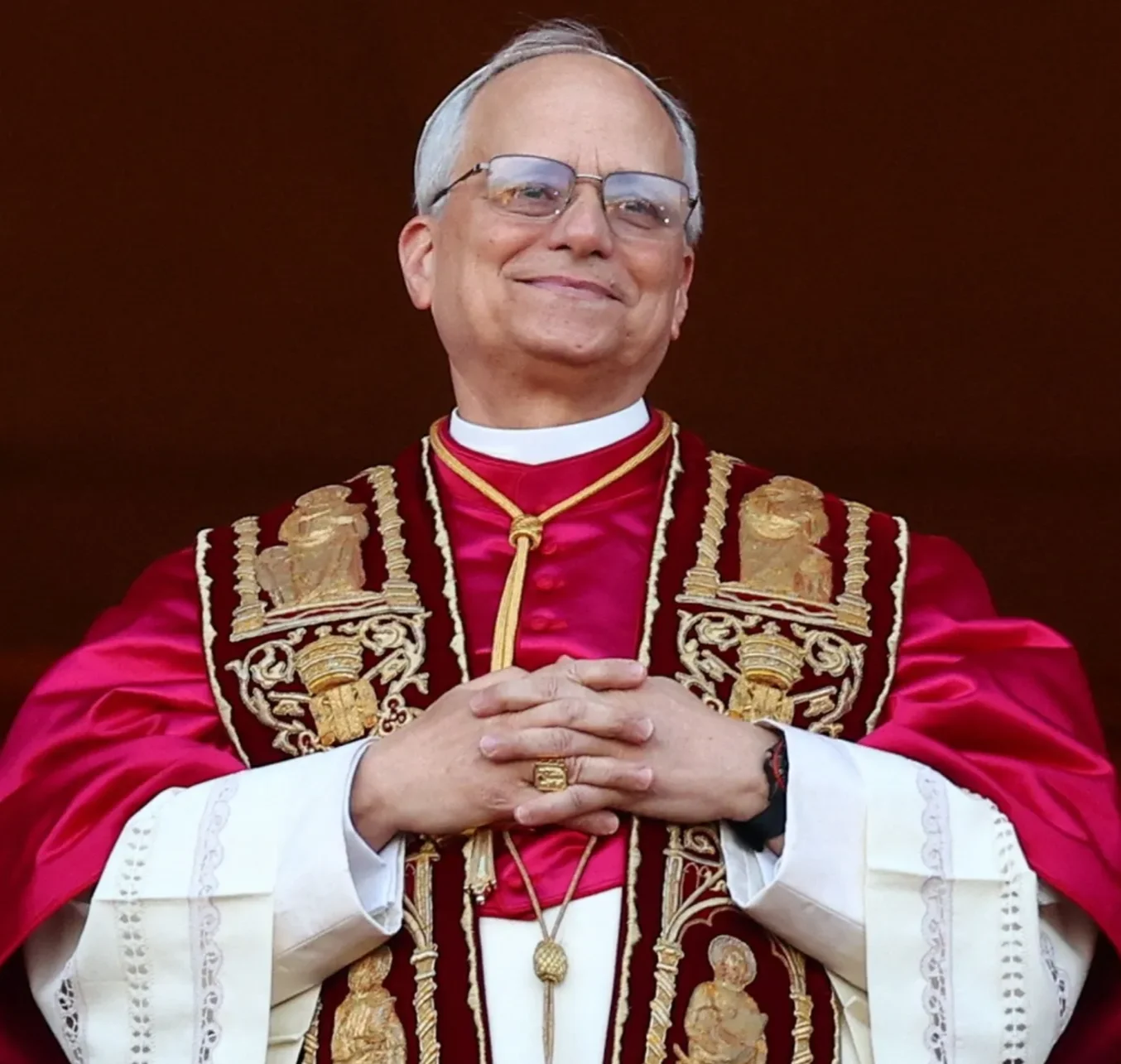 Papa Leão XIV sorri com as mãos entrelaçadas, vestindo murça vermelha e estola bordada