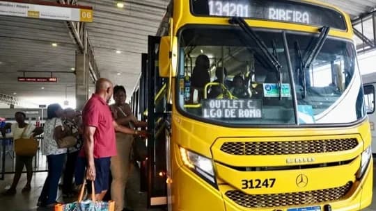 Passageiros embarcam em ônibus amarelo em estação de Salvador