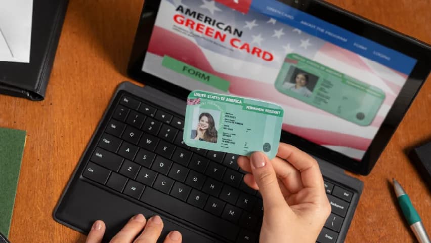 Pessoa segura um green card diante de um site sobre o documento