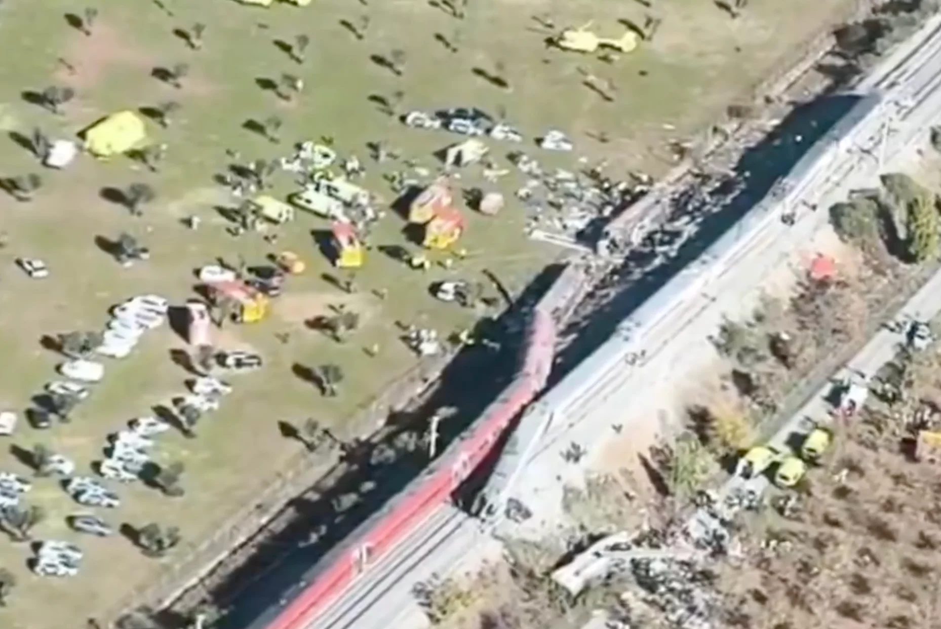 Vista aérea de trem descarrilado e equipes de resgate ao lado da ferrovia